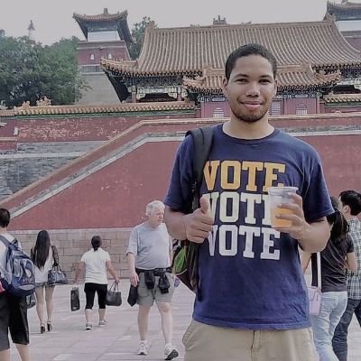 He is posing with a thumbsup and a shirt that says Vote three times.